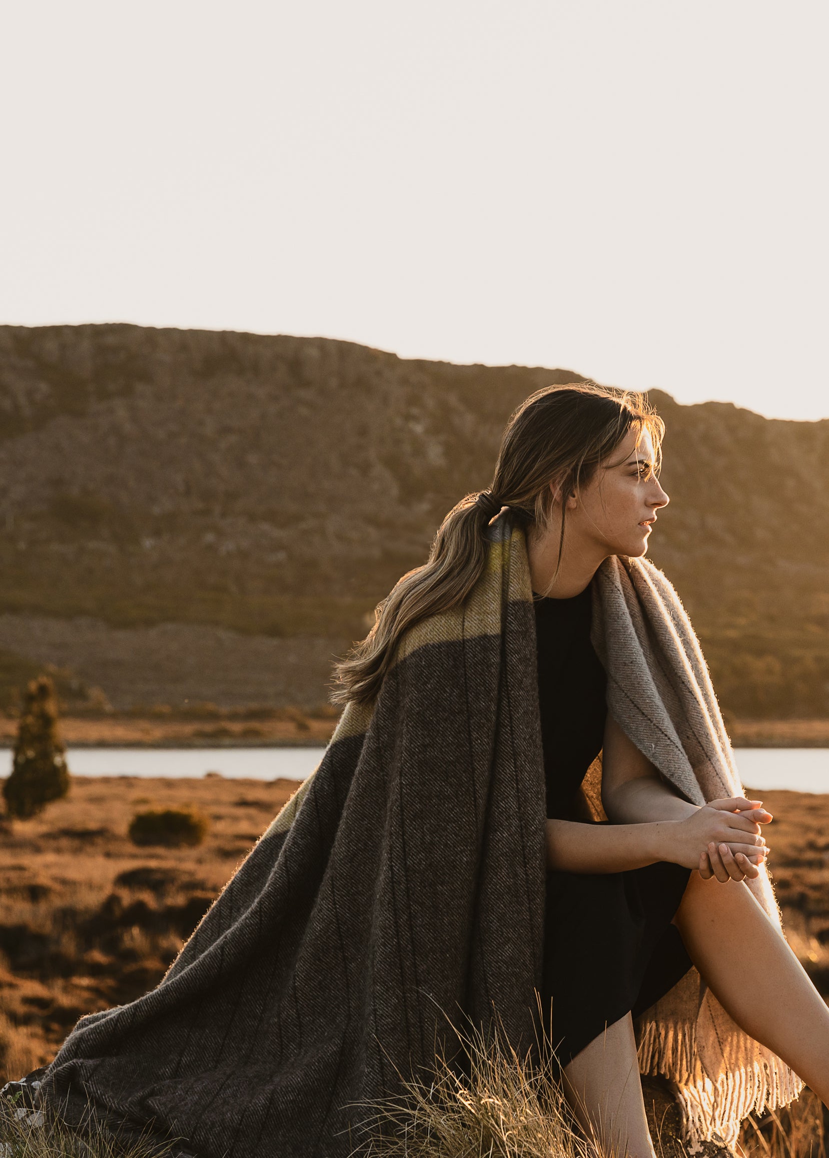 A girl sitting with the Cradle Mountain throw over her shoulders.