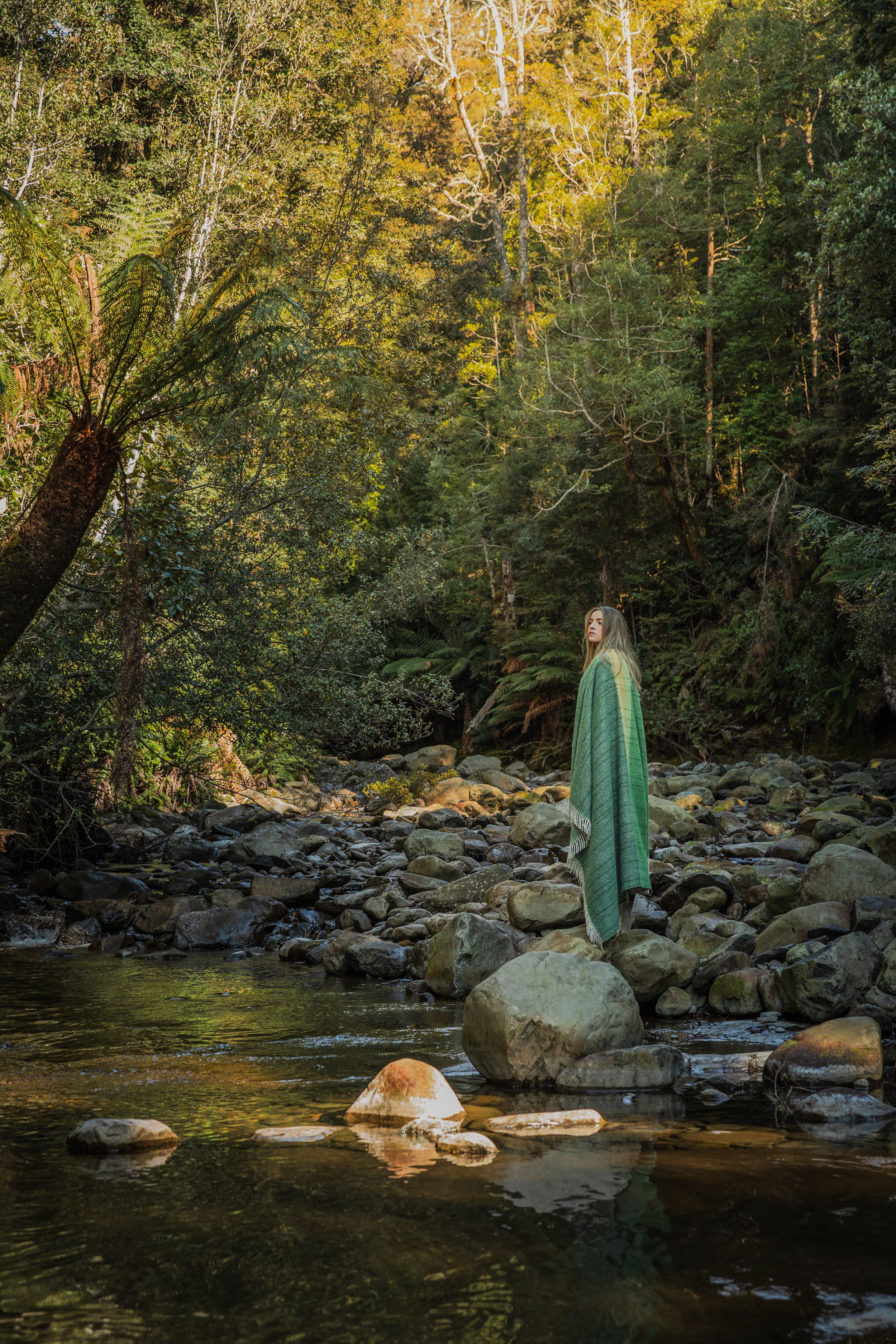 A girl wrapped in the Tarkine Forest throw standing in a river in the Tarkine.