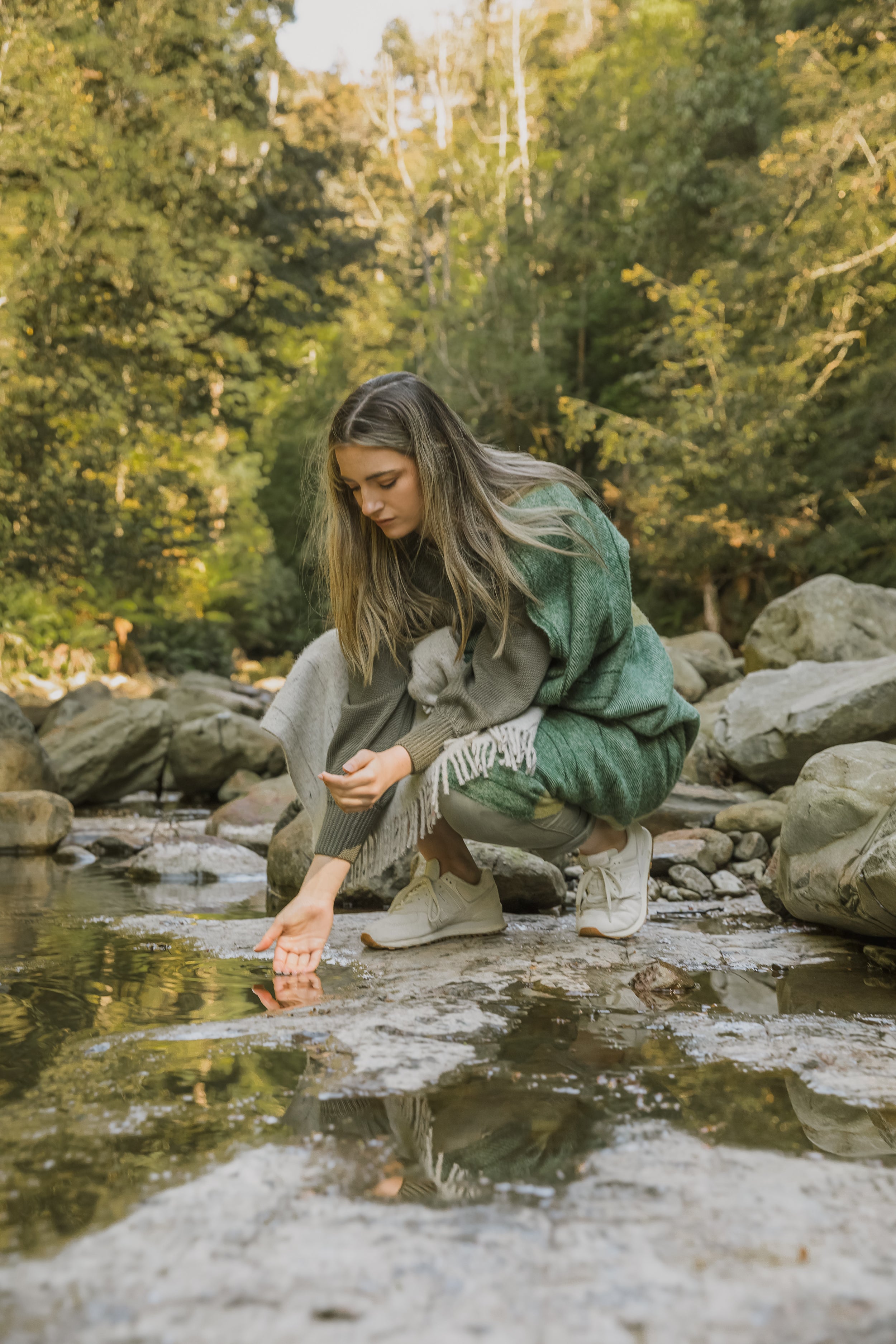 A girl wrapped in the Tarkine Forest throw crouched by the water.