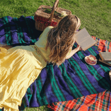 A young woman in a yellow dress reading a book on a Blackwatch Tartan picnic rug.