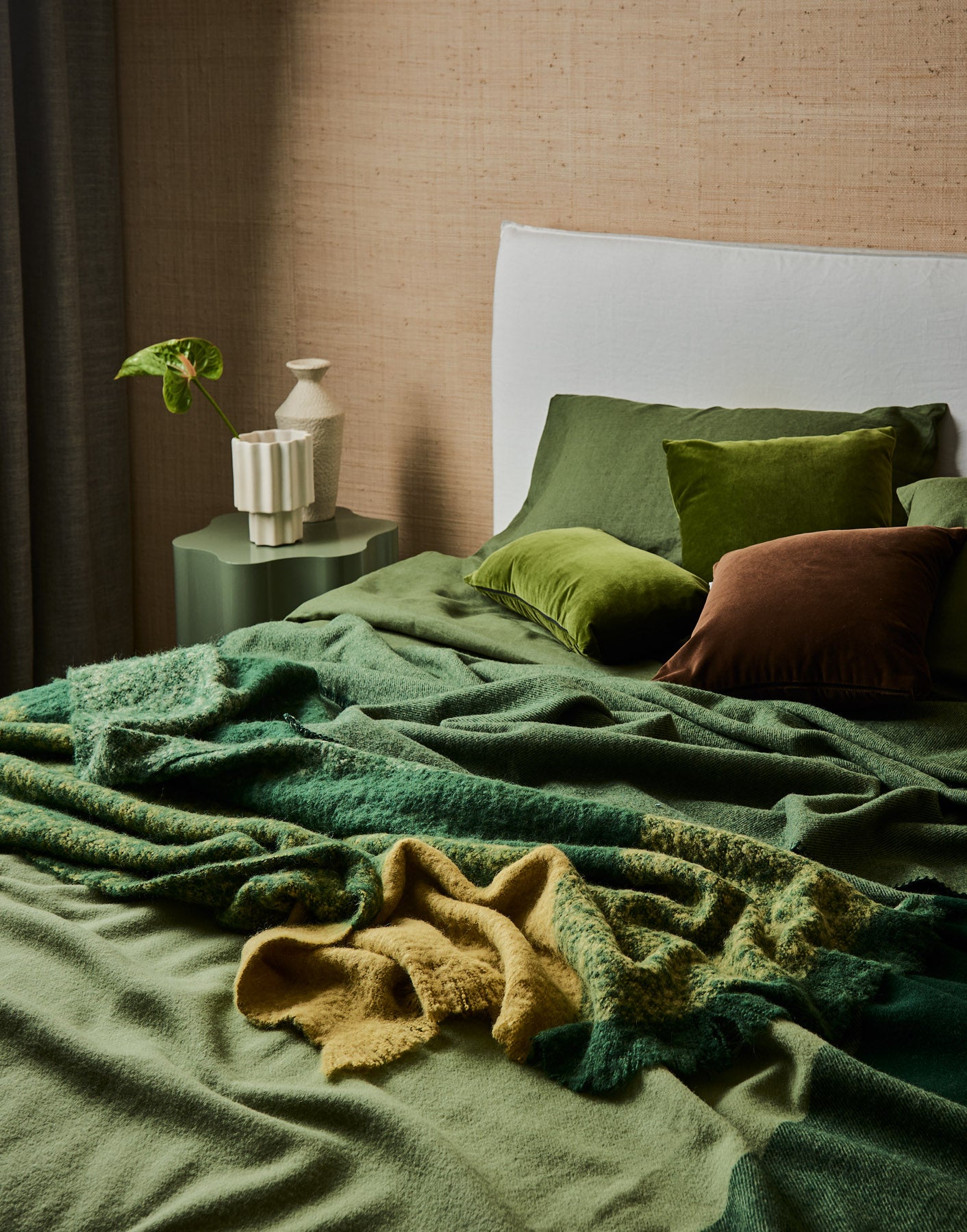 A cosy green sanctuary of an unmade bed featuring the Geo blanket and Lustre throws in forest.