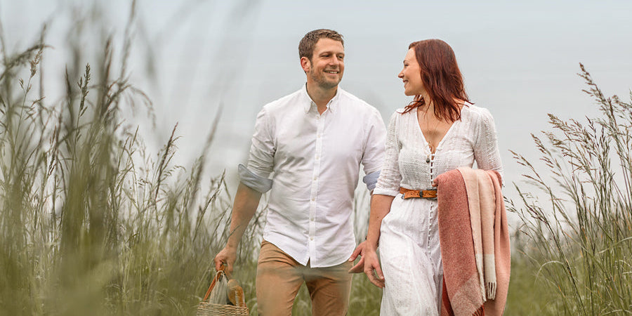 A couple dressed in white, walking through long grass with a Waverley Mills picnic rug.