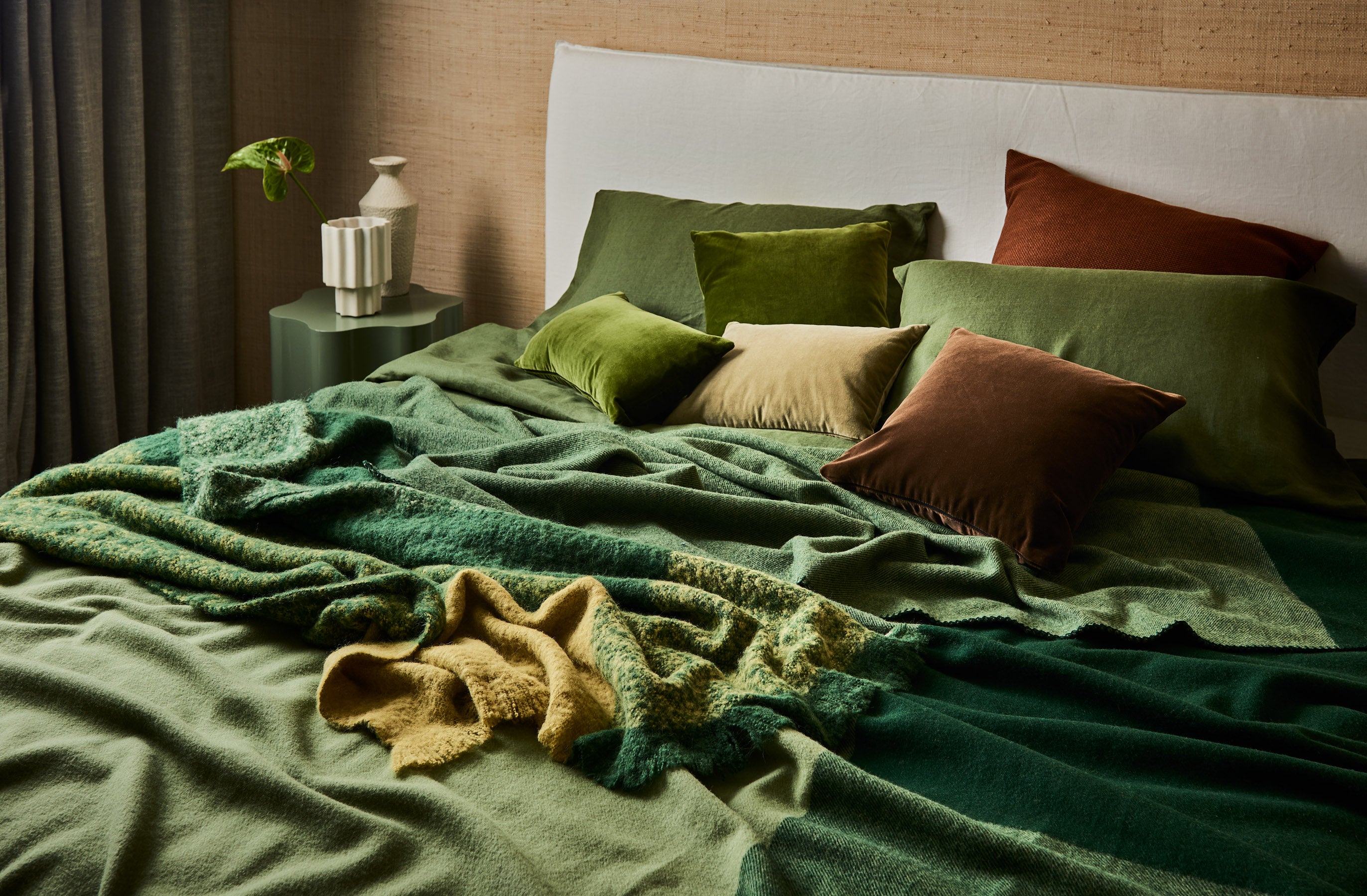 A modern style bed dressed with a merino wool blanket and alpaca throw in tones of green.