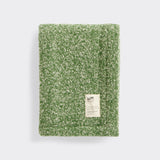 A folded green and natural baby blanket made with cormo wool.