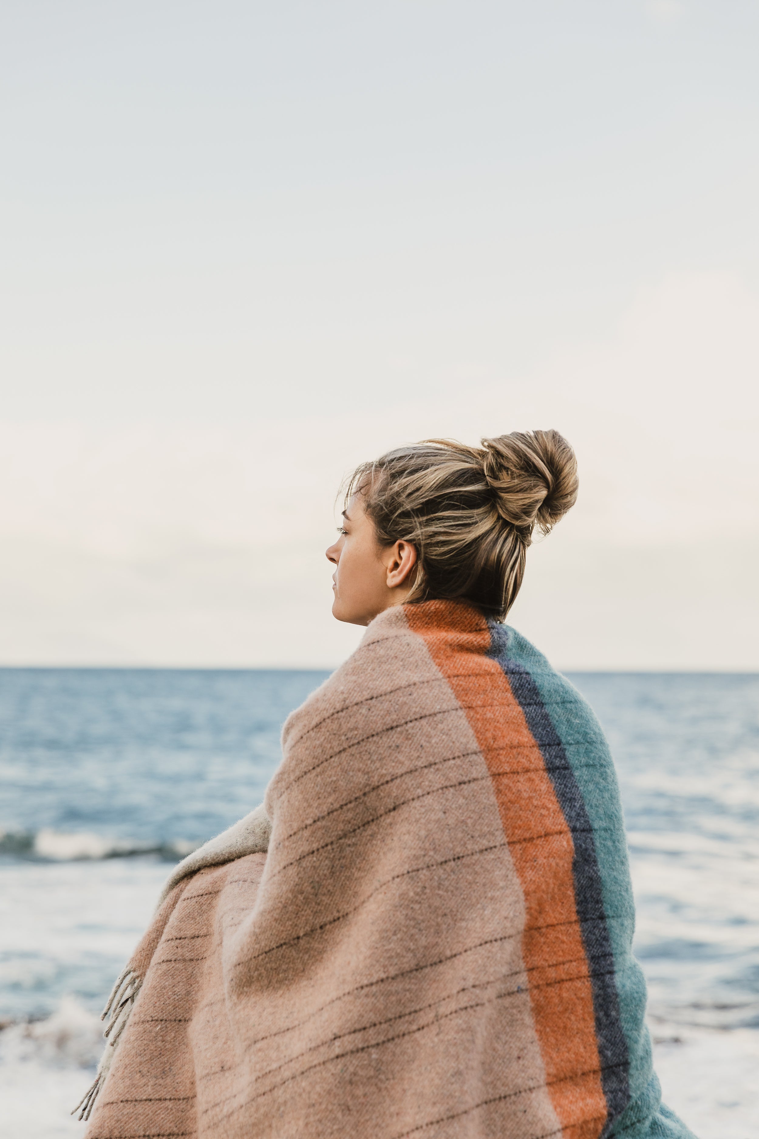 A girl wrapped in the Bay of Fires throw by the sea.