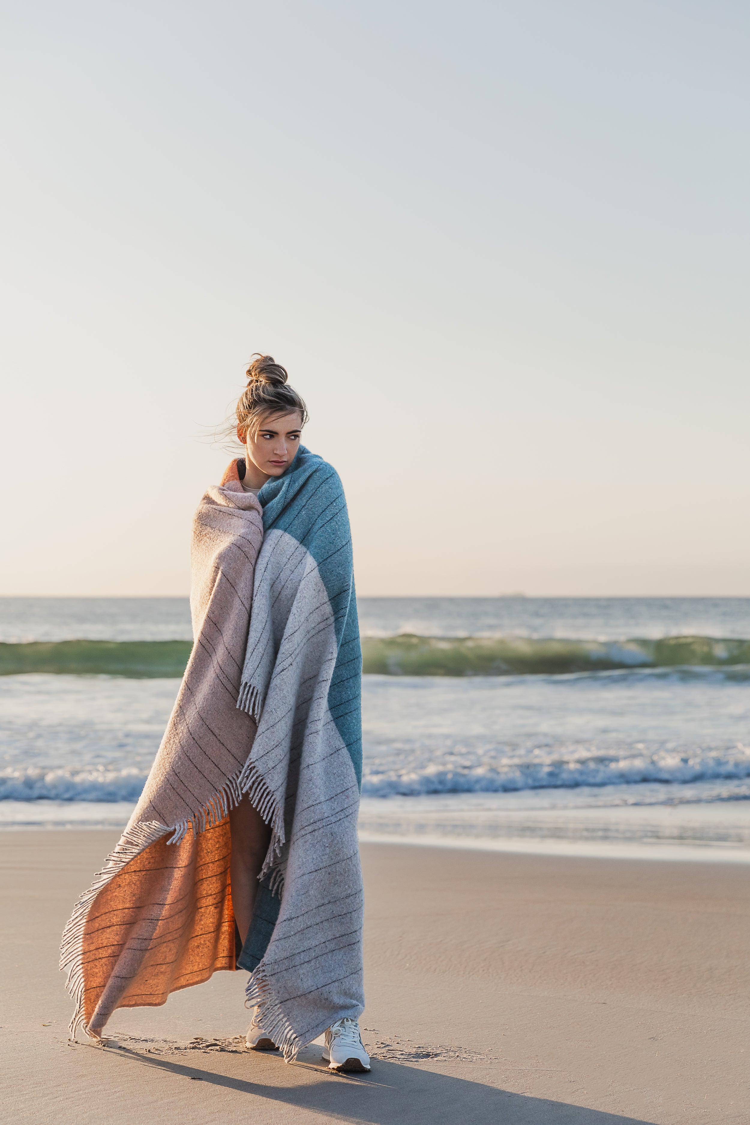 A girl wrapped in the Bay of Fires throw on the beach.