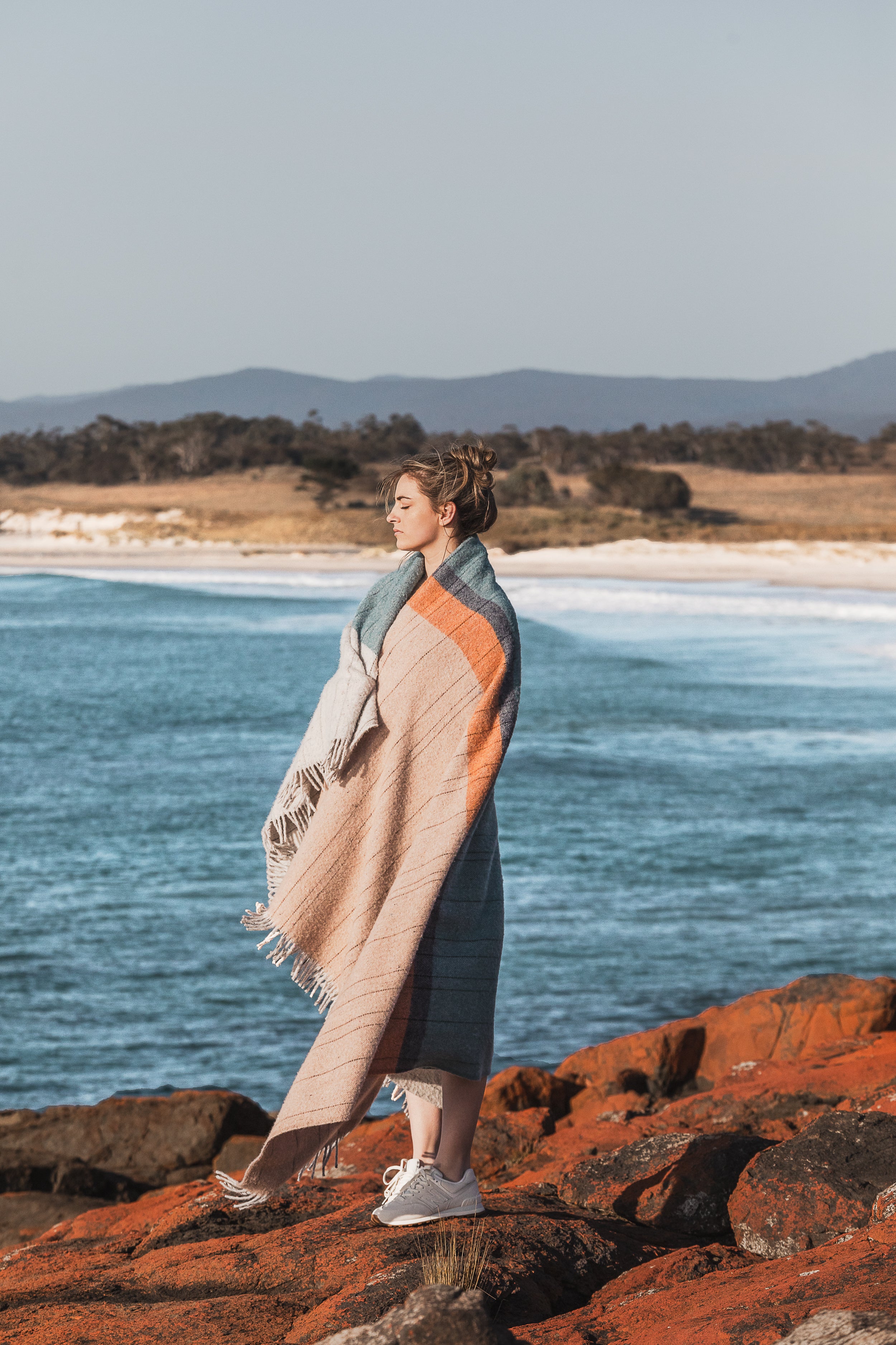 A girl wrapped in the Bay of Fires throw on the lichen covered rocks.