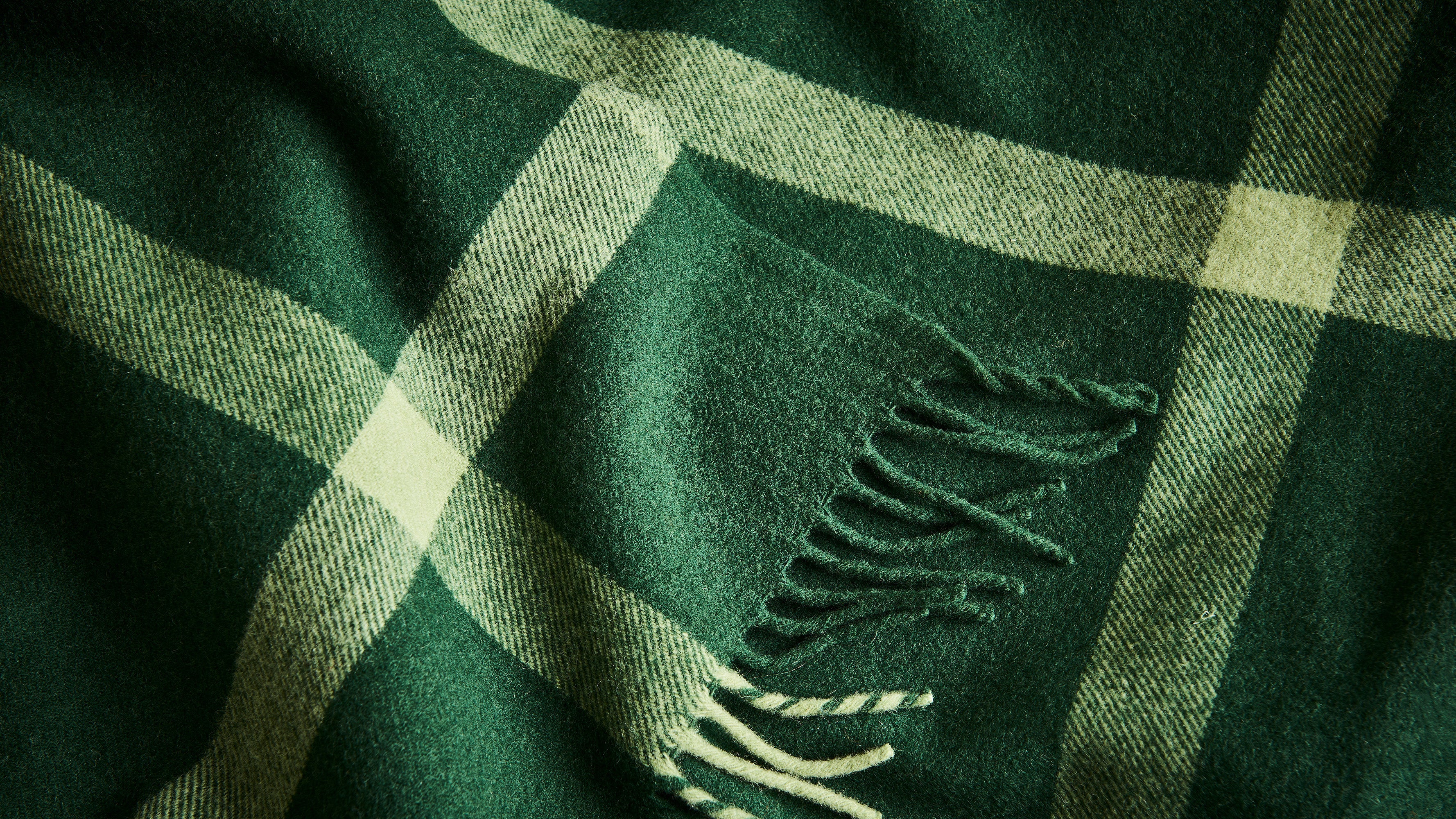A close up of the green ravine throw displaying the texture of the woollen weave and striped pattern.