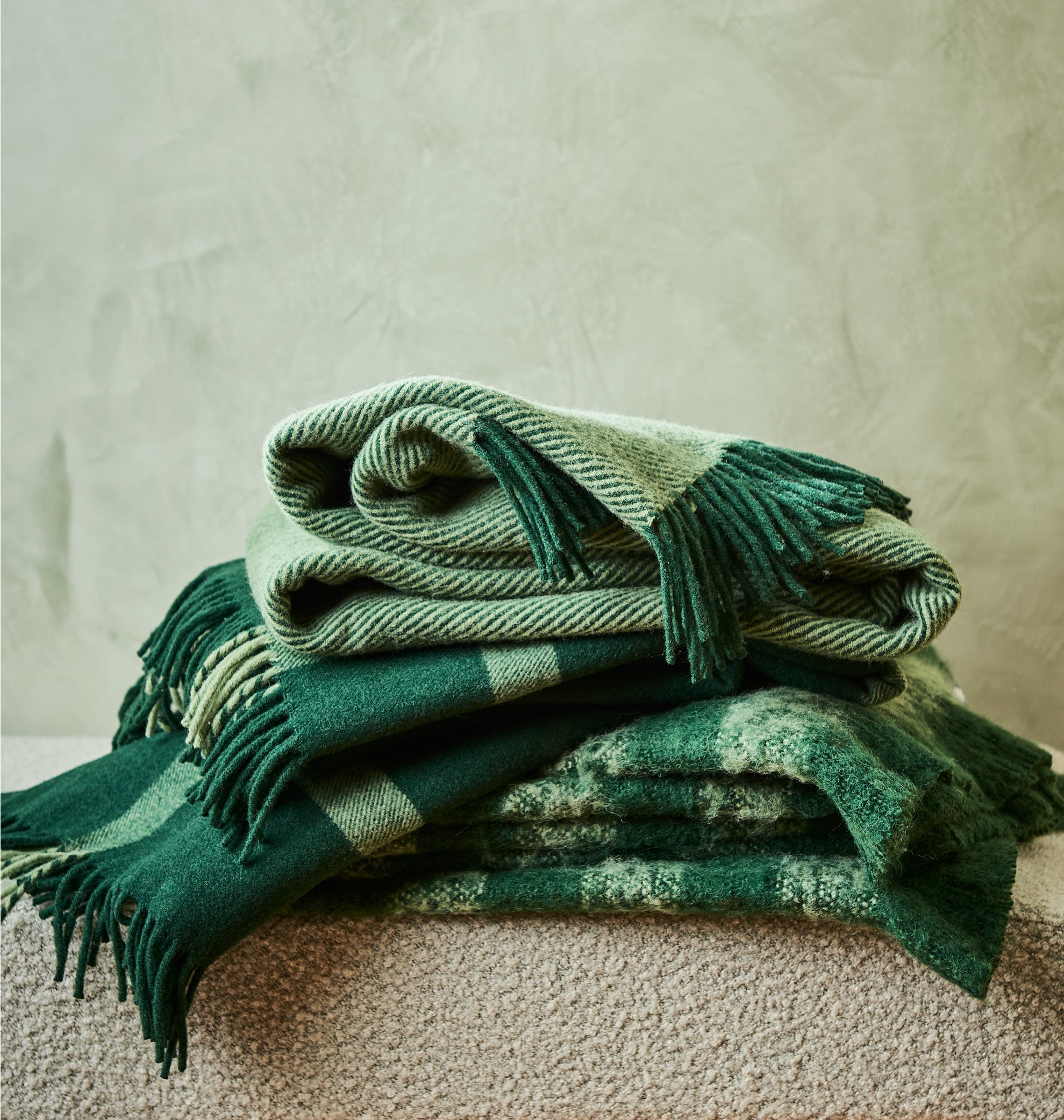 A stack of three green throws showing complimentary tones together.