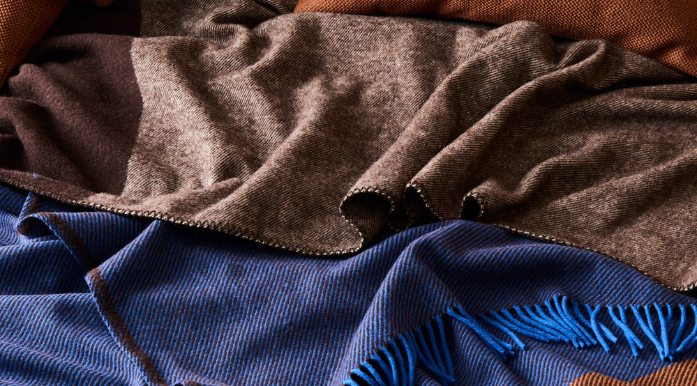 A roughly made bed using the geo blanket in umber and draped with a gem throw in cobalt.