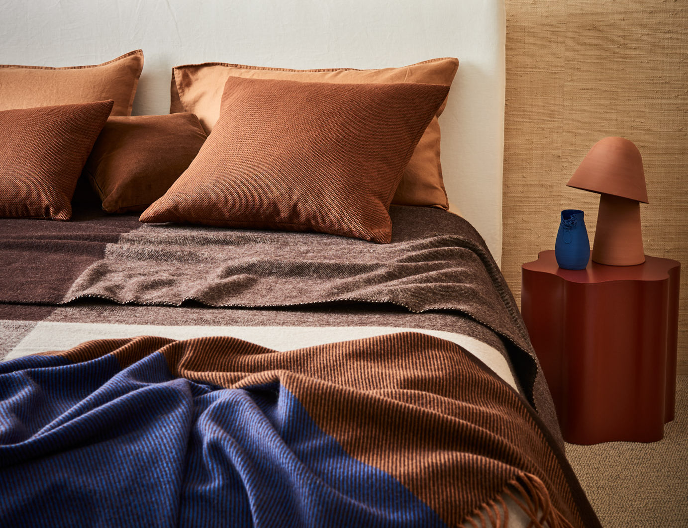 A modern styled bed made up with a geo blanket in umber and gem throw in cobalt.