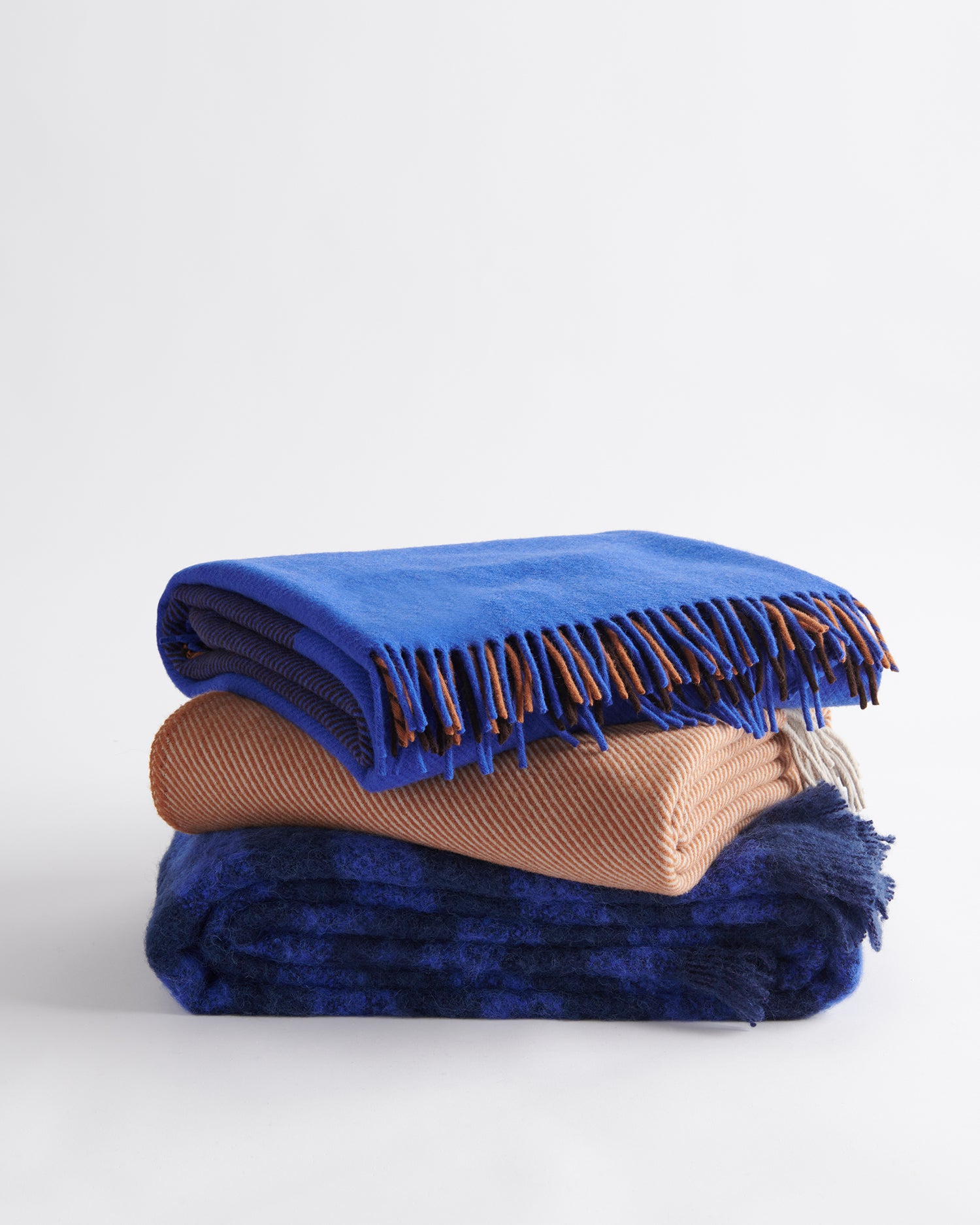 A stack of three complementary throws; gem in cobalt, diagonal in terracotta, rift in cobalt.