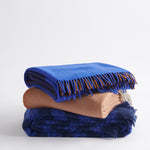 A stack of three throws including; Gem in cobalt, Diagonal in terracotta, and Rift in cobalt.