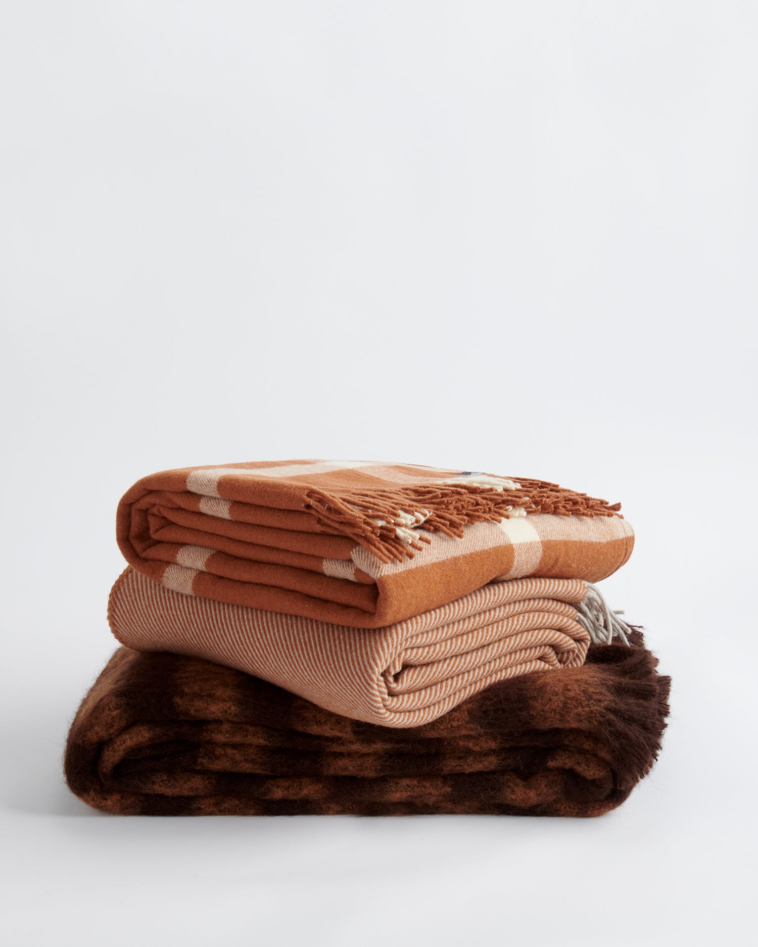 A stack of three throws including the ravine throw, diagonal throw and rift throw all in terracotta.
