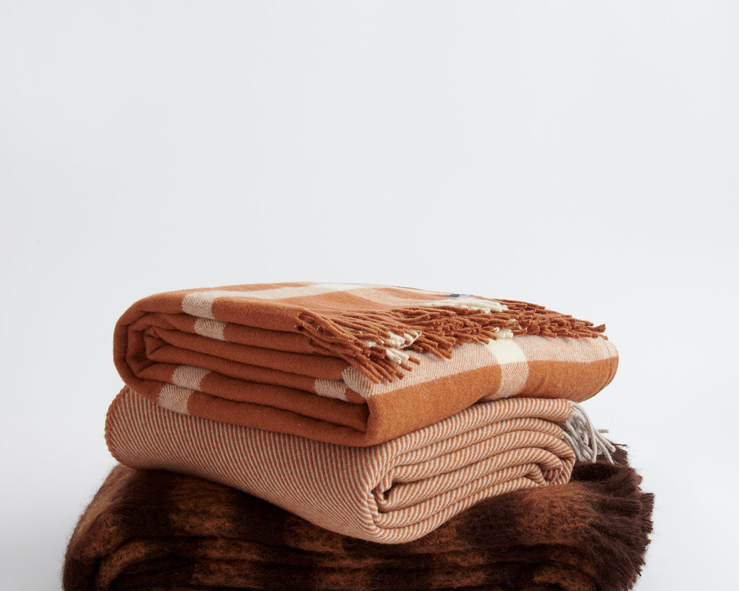 Stack of three throws including Ravine in terracotta, Diagonal in terracotta, and Rift in terracotta.