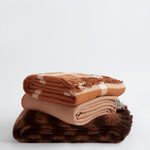 Stack of three throws including Ravine in terracotta, Diagonal in terracotta, and Rift in terracotta.