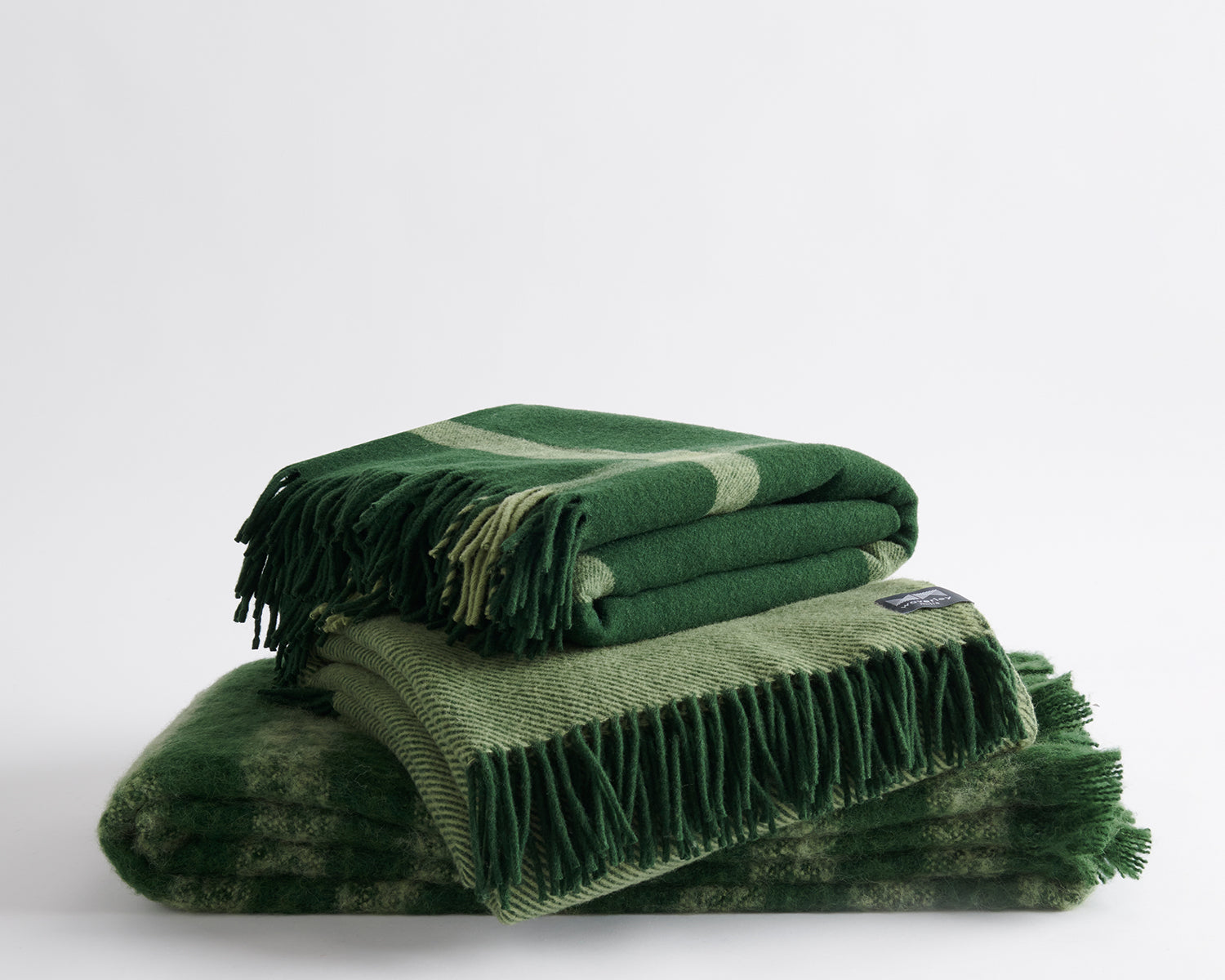 A trio of folded throws including; Ravine in forest, Diagonal in forest, and Rift in forest.
