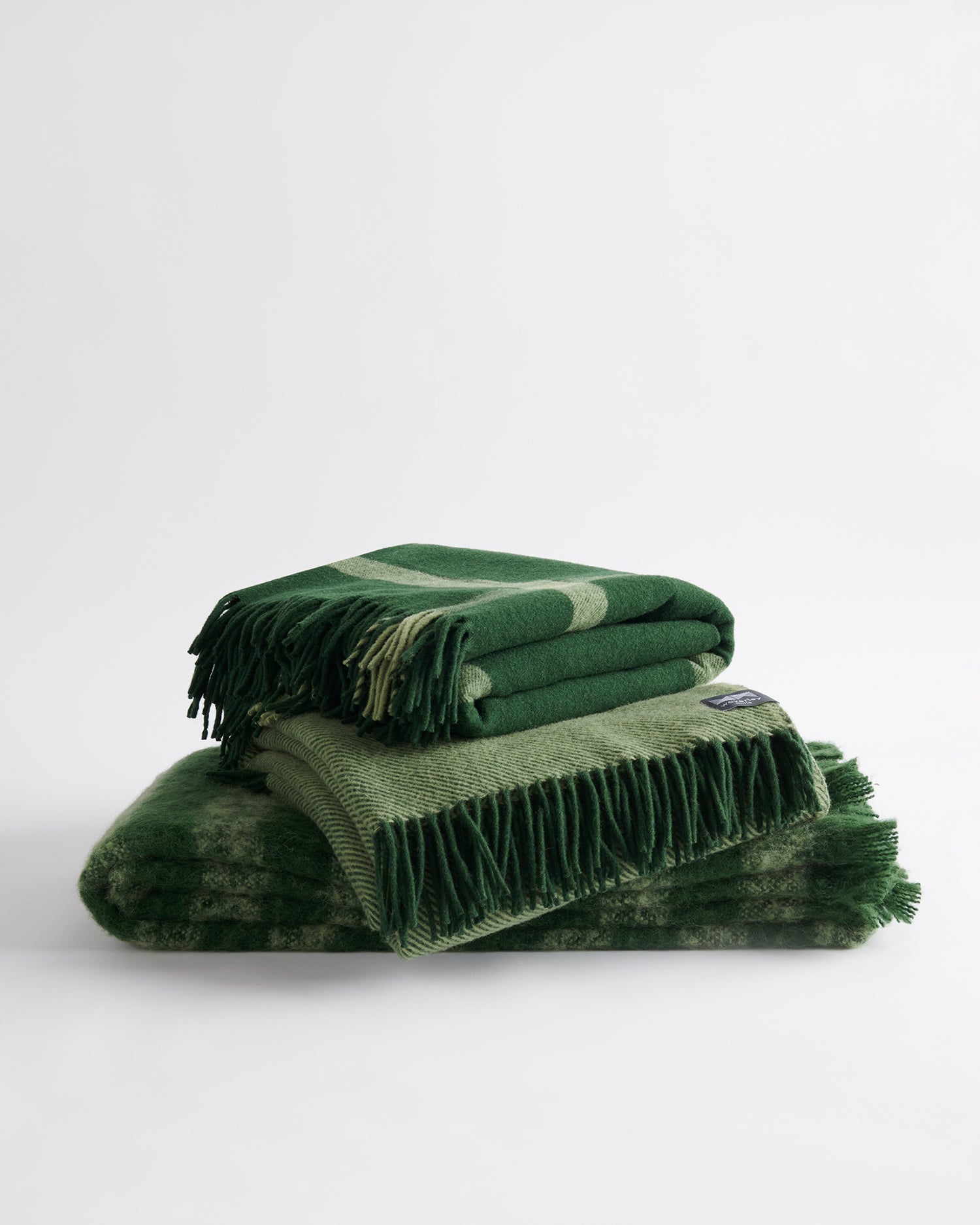 A trio of folded throws including; Ravine in forest, Diagonal in forest, and Rift in forest.