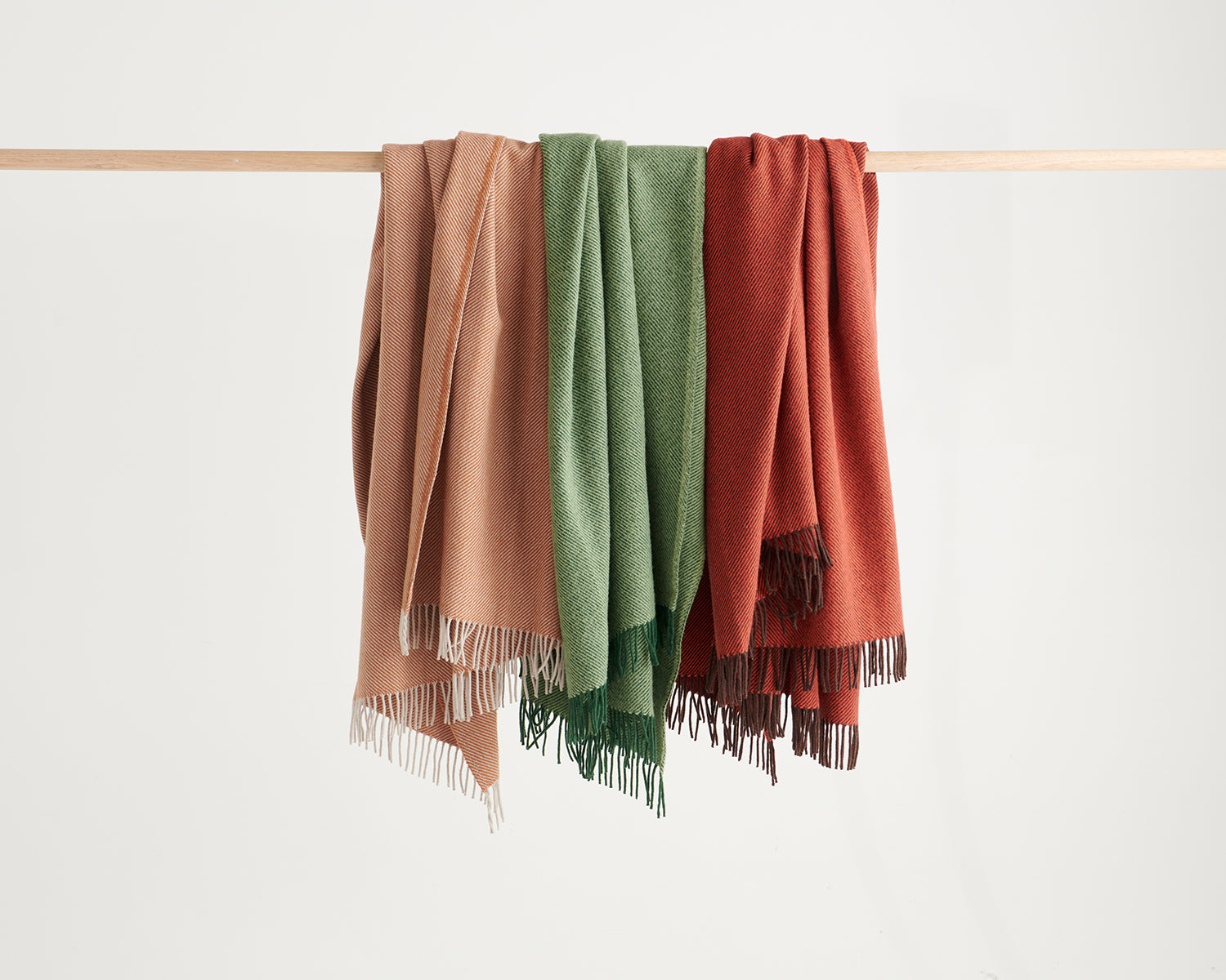 Three diagonal throws hanging side by side in terracotta, forest and umber colourways.