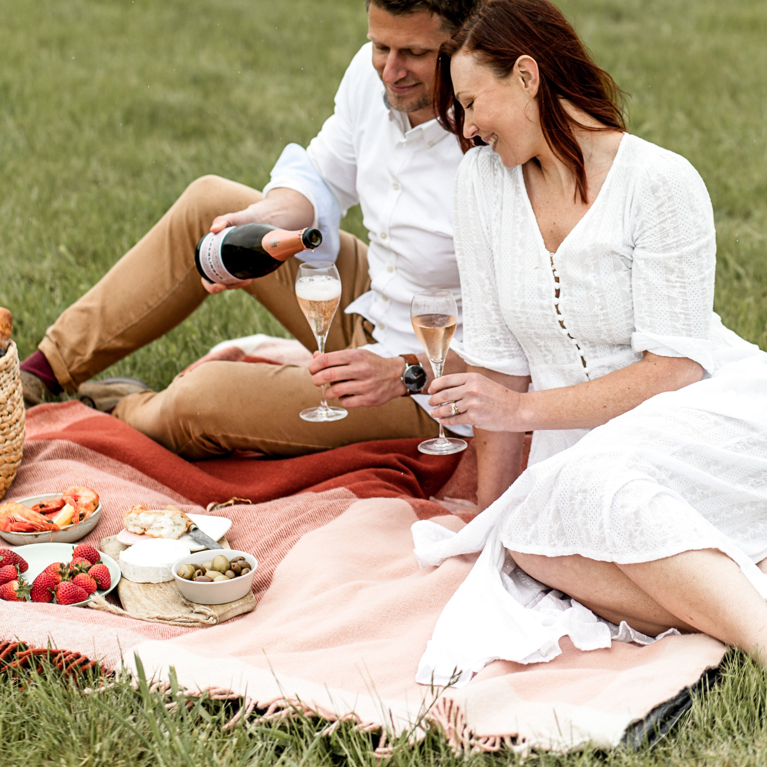 A couple picnicking on the grass, using a graze picnic rug in pink.