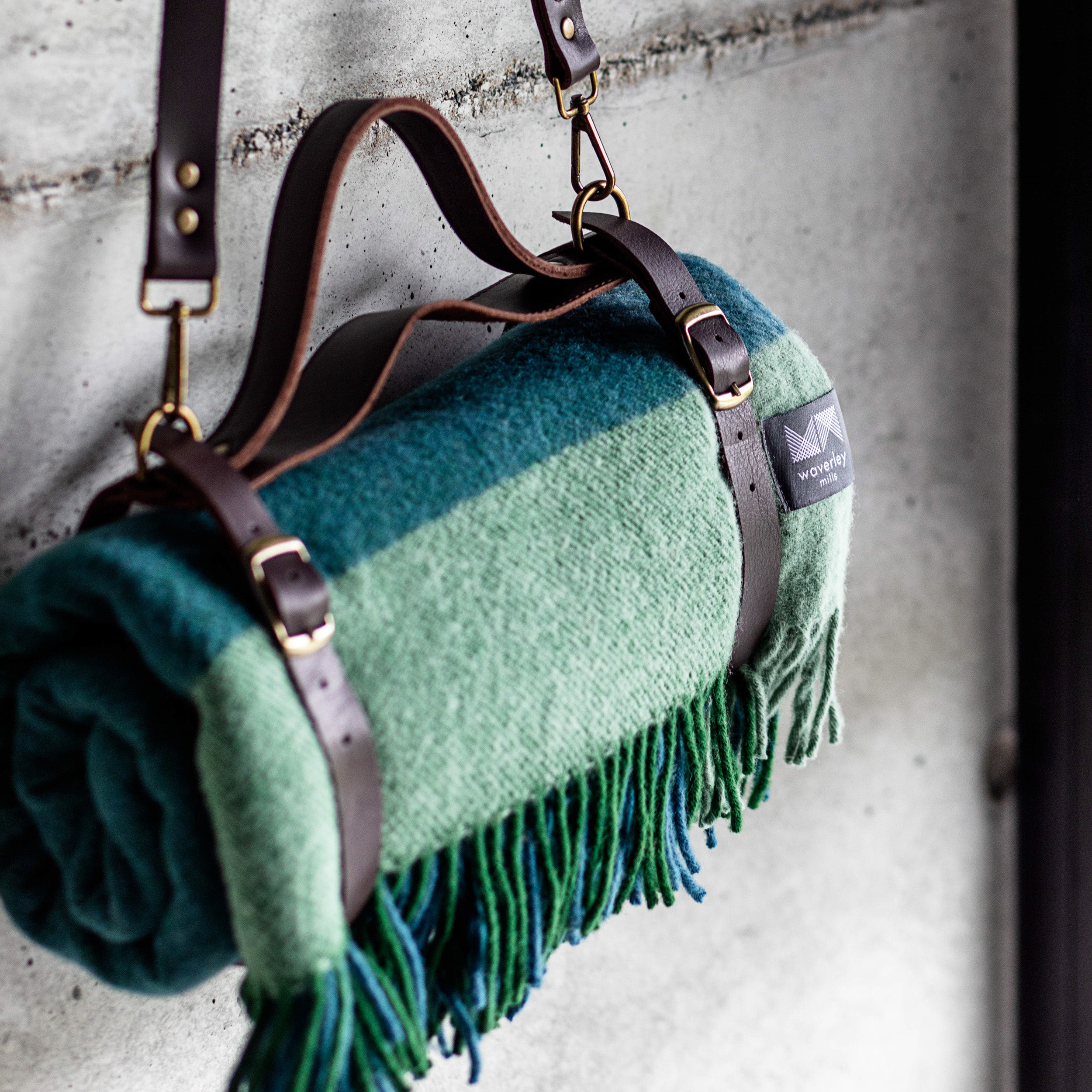 A rolled green and blue graze picnic rug in a brown leather carrier.