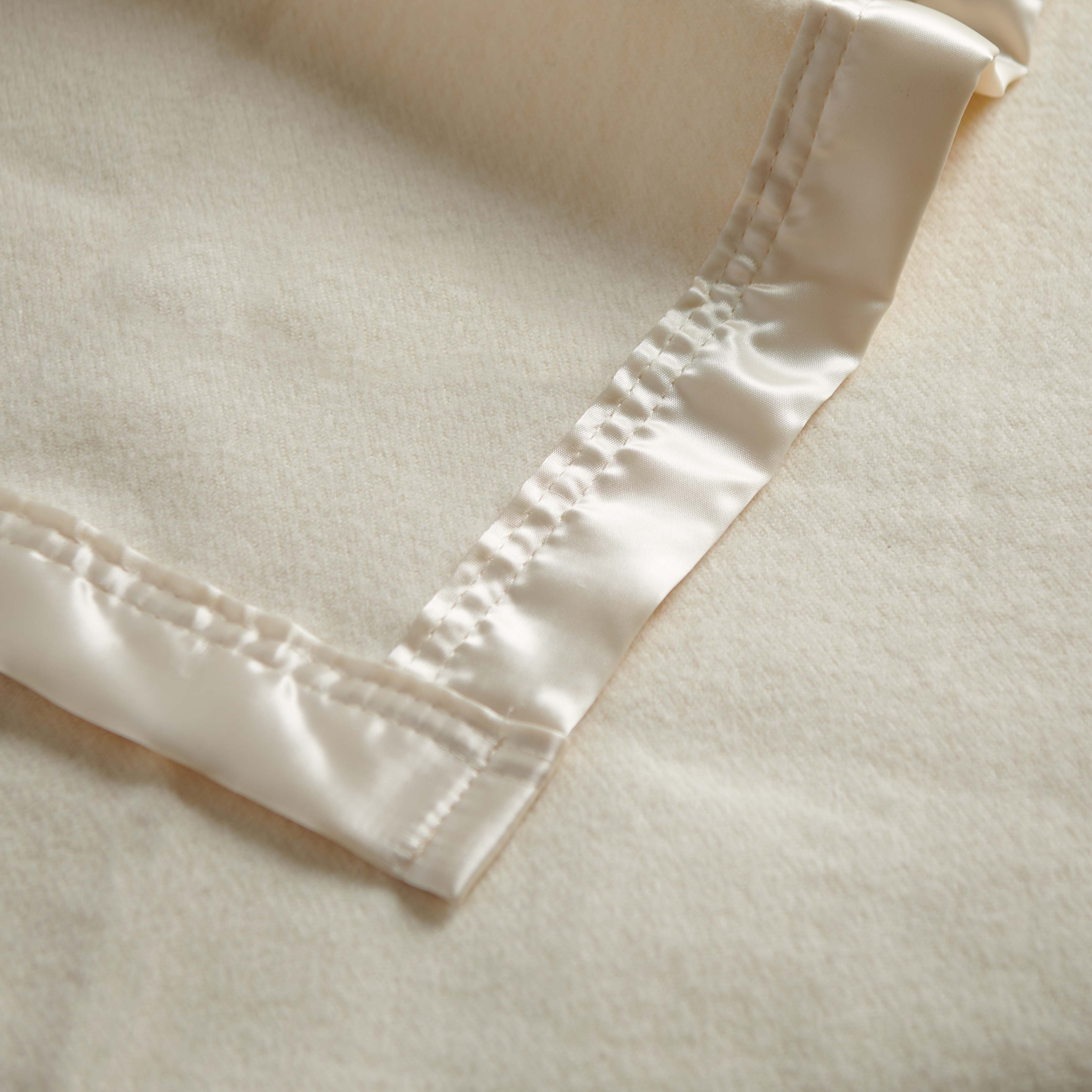 Close up of a natural merino nursery blanket with satin edge.