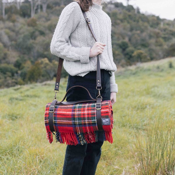 A woman holding a Royal Stewart picnic rug in a leather carrier with shoulder strap.